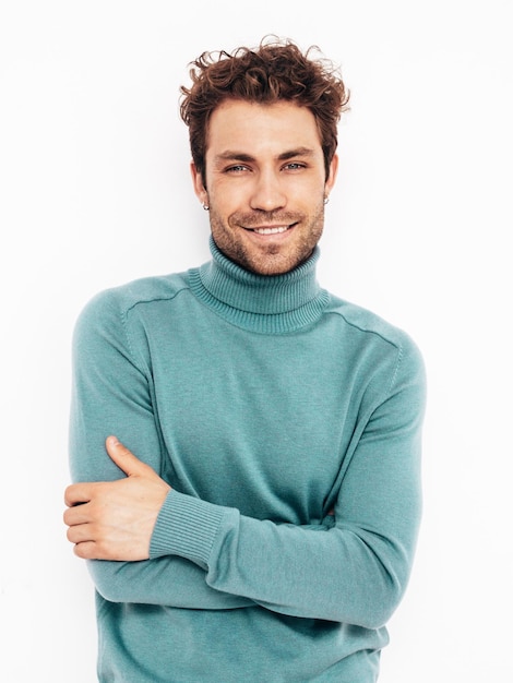Portrait of handsome confident model Sexy stylish man dressed in blue sweater and jeans Fashion hipster male with curly hairstyle posing near white wall in studio Isolated