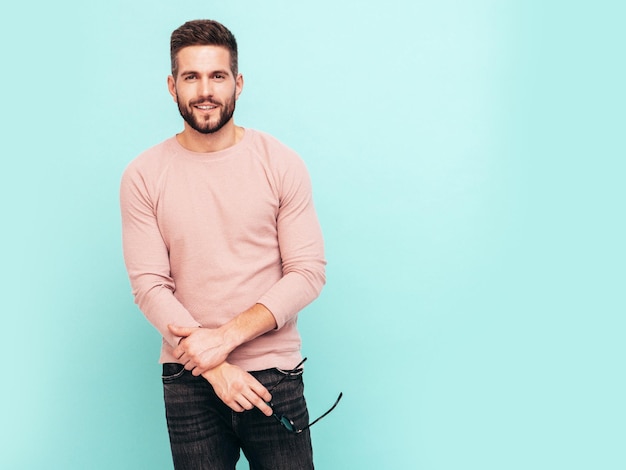 Portrait of handsome confident model Sexy stylish man dressed in pink sweater and jeans Fashion hipster male posing near blue wall in studio In sunglasses Isolated