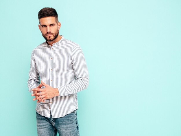 Portrait of handsome confident model Sexy stylish man dressed in shirt and jeans Fashion hipster male posing near blue wall in studio