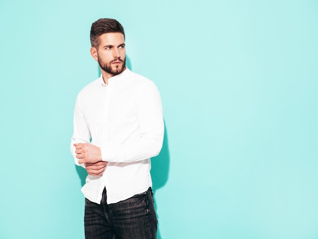 Portrait of handsome confident model Sexy stylish man dressed in white shirt and jeans Fashion hipster male posing near blue wall in studio Isolated