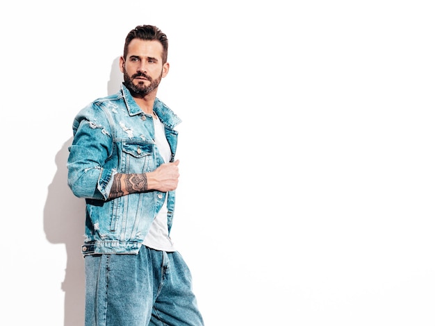 Ritratto di modello lambersexual bello fiducioso elegante hipster uomo sexy vestito con giacca di jeans moda maschile isolato sul muro bianco in studio