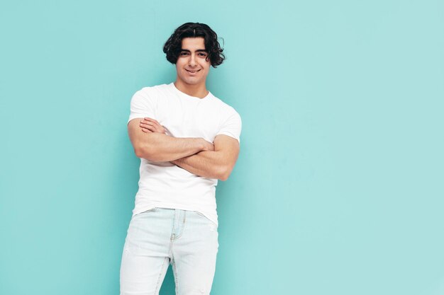 잘 생긴 자신감 세련된 힙스터 램버섹슈얼 모델의 초상화 여름 흰색 티셔츠와 청바지 옷을 입은 섹시한 남자 패션 남성 스튜디오에서 격리 파란색 벽 근처 포즈