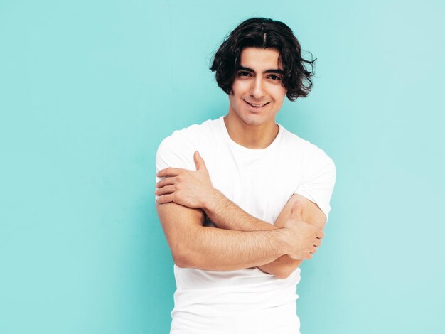 Portrait of handsome confident stylish hipster lambersexual model Sexy man dressed in summer white Tshirt and jeans clothes Fashion male isolated in studio Posing near blue wall