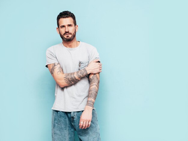 Portrait of handsome confident stylish hipster lambersexual model Sexy man dressed in Tshirt and jeans Fashion male isolated on blue wall in studio