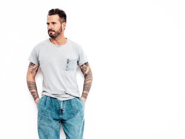 ハンサムな自信を持ってスタイリッシュなヒップスターランバーセクシャルモデルの肖像画Tシャツとジーンズに身を包んだセクシーな男性スタジオの白い壁に分離されたファッションの男性