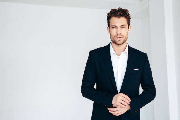 Portrait of handsome confident stylish hipster lambersexual model Sexy modern man dressed in black elegant suit Fashion male posing in studio on white background