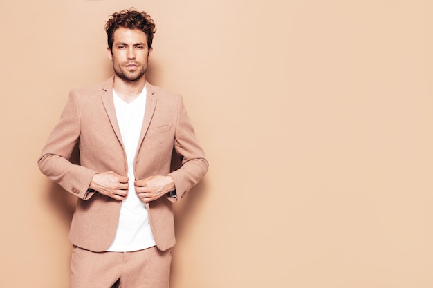 Portrait of handsome confident stylish hipster lambersexual model Sexy modern man dressed in elegant beige suit Fashion male with curly hairstyle posing in studio Isolated