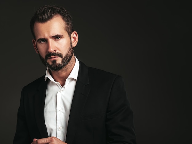 Portrait of handsome confident stylish hipster lambersexual model Sexy modern man dressed in elegant black suit Fashion male posing in studio on dark background Looking at camera