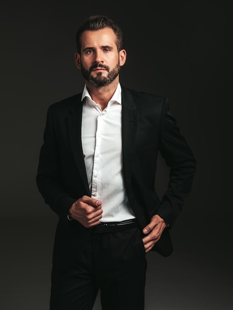 Free photo portrait of handsome confident stylish hipster lambersexual model sexy modern man dressed in elegant black suit fashion male posing in studio on dark background