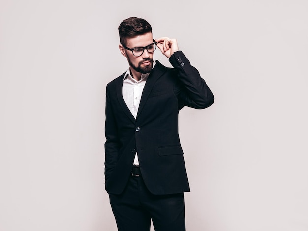 Portrait of handsome confident stylish hipster lambersexual model Sexy modern man dressed in elegant black suit Fashion male posing in studio Isolated on grey