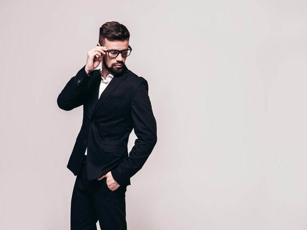 잘 생긴 자신감 세련된 힙스터 램버섹슈얼 모델의 초상화 우아한 검은 양복을 입은 섹시한 현대 남자 패션 남성 회색에 격리 된 흰색 벽 근처 스튜디오에서 포즈