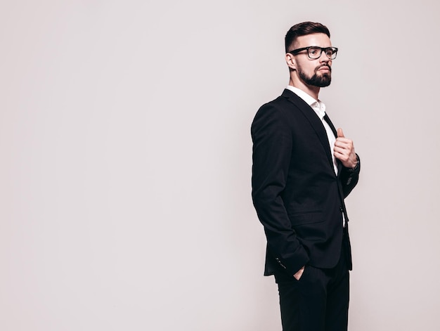 Portrait of handsome confident stylish hipster lambersexual model Sexy modern man dressed in elegant black suit Fashion male posing in studio near white wall Isolated on grey