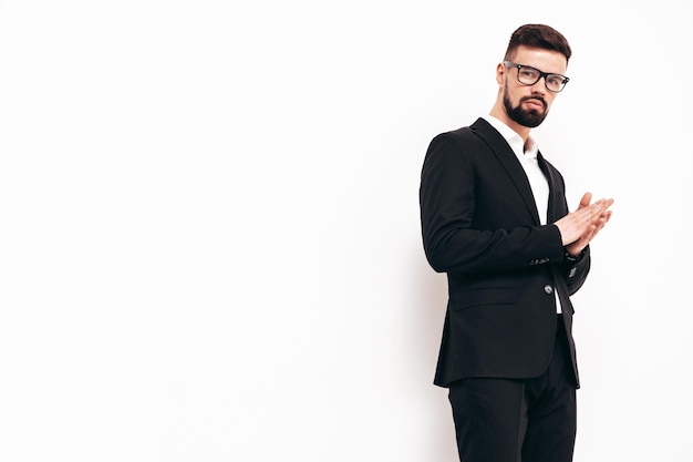 Portrait of handsome confident stylish hipster lambersexual model Sexy modern man dressed in elegant black suit Fashion male posing in studio near white wall Isolated