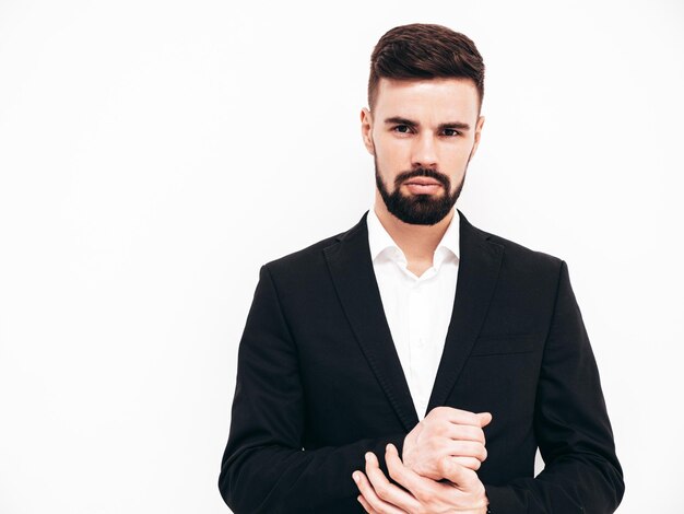 Portrait of handsome confident stylish hipster lambersexual model Sexy modern man dressed in elegant black suit Fashion male posing in studio near white wall Isolated