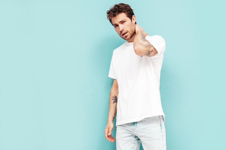 Free Photo portrait of handsome confident stylish hipster lambersexual model with curly hairstyle sexy man dressed in jeans and white tshirt fashion male isolated on blue wall in studio