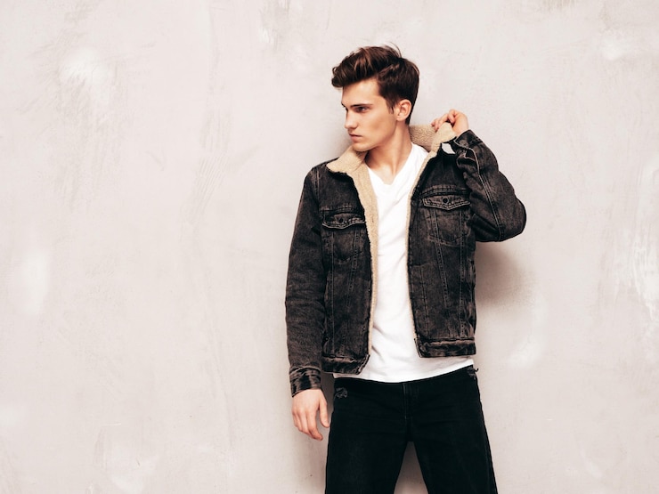 Free Photo portrait of handsome confident stylish hipster lambersexual modelman dressed in black jacket and jeans fashion male posing in studio near grey wall