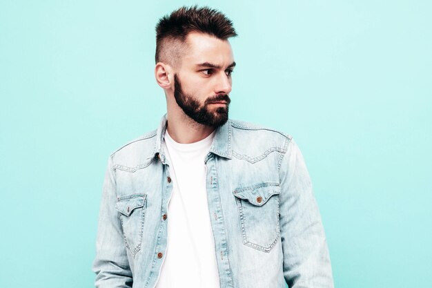 Portrait of handsome confident stylish hipster lambersexual modelMan dressed in jacket and jeans Fashion male posing near blue wall in studio