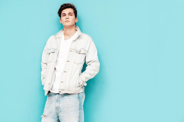 Portrait of handsome confident stylish hipster lambersexual modelMan dressed in jacket and jeans Fashion male posing in studio near blue wall