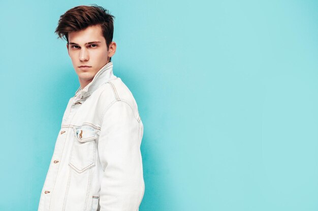 Portrait of handsome confident stylish hipster lambersexual modelMan dressed in jacket and jeans Fashion male posing in studio near blue wall