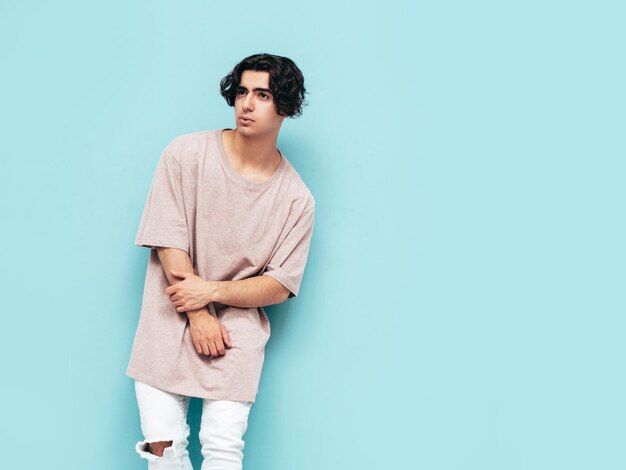 Portrait of handsome confident stylish hipster lambersexual modelMan dressed in over size Tshirt and jeans Fashion male isolated in studio Posing near blue wall