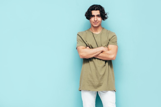 Free photo portrait of handsome confident stylish hipster lambersexual modelman dressed in over size tshirt and jeans fashion male isolated in studio posing near blue wall