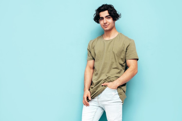 Free photo portrait of handsome confident stylish hipster lambersexual modelman dressed in over size tshirt and jeans fashion male isolated in studio posing near blue wall
