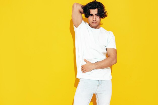 Portrait of handsome confident stylish hipster lambersexual modelMan dressed in over size Tshirt and jeans Fashion male isolated in studio Posing near yellow wall