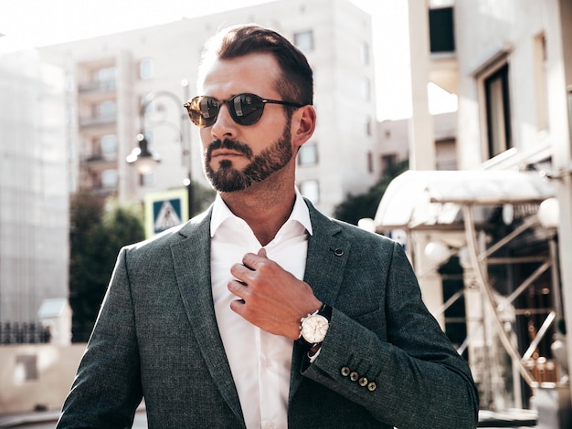 Portrait of handsome confident stylish hipster lambersexual modelModern man dressed in elegant suit Fashion male posing in the street background in Europe city at sunset In sunglasses