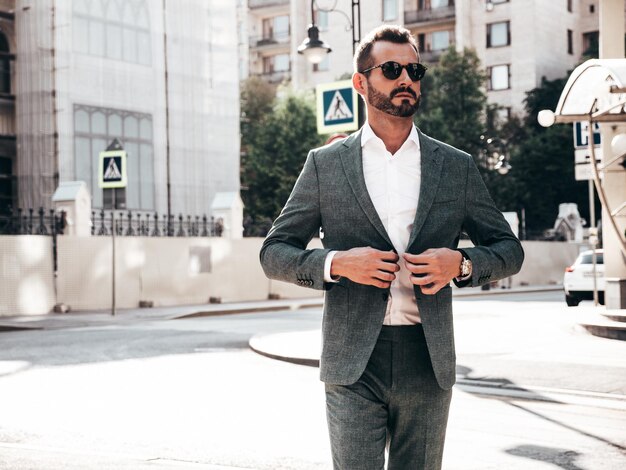 Portrait of handsome confident stylish hipster lambersexual modelSexy modern man dressed in elegant suit Fashion male posing in the street background in Europe city at sunset In sunglasses