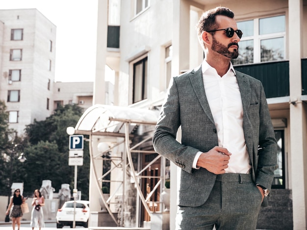 Portrait of handsome confident stylish hipster lambersexual modelSexy modern man dressed in elegant suit Fashion male posing in the street background in Europe city at sunset In sunglasses