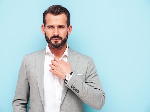 Portrait of handsome confident stylish hipster lambersexual modelSexy modern man dressed in elegant suit Fashion male posing in studio near blue wall Looking at camera