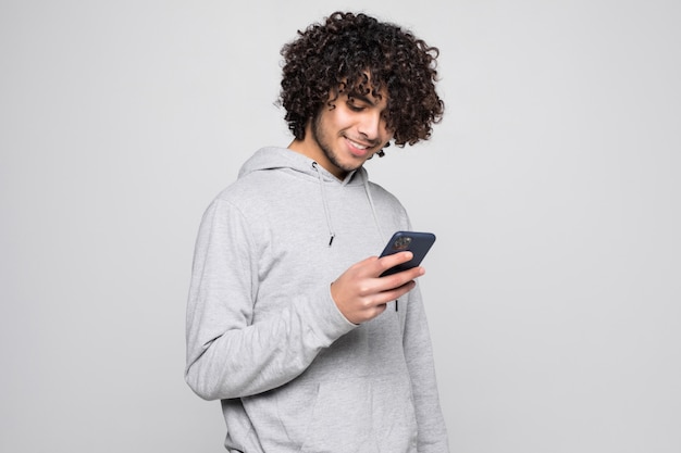 Portrait of handsome curly man holding phone isolated on white wall