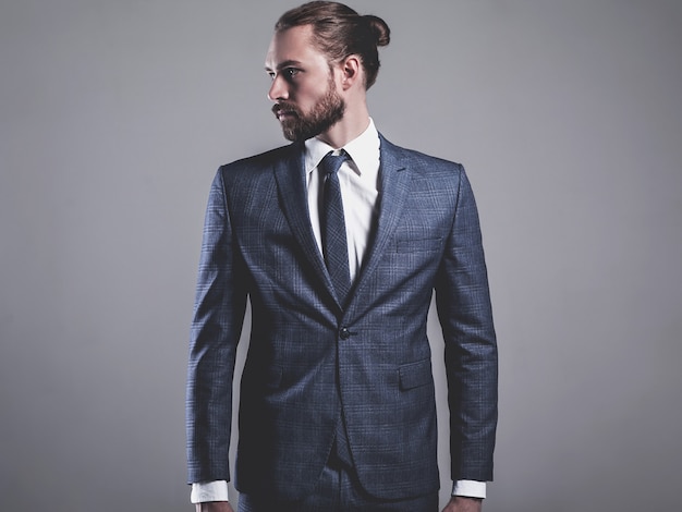 Портрет красивый модный бизнесмен модель, одетый в элегантный синий костюм в очках позирует на сером
