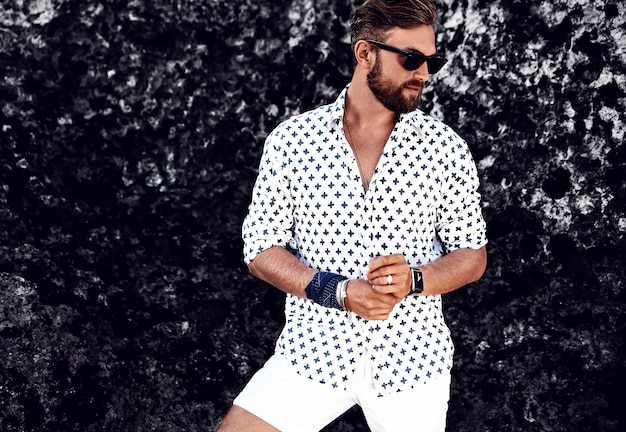 Free photo portrait of handsome fashion man model wearing white clothes posing near rocks on the beach