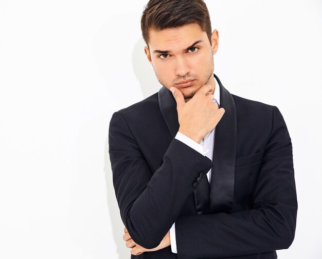 portrait of handsome fashion stylish businessman model dressed in elegant black classic suit. Touching his chin