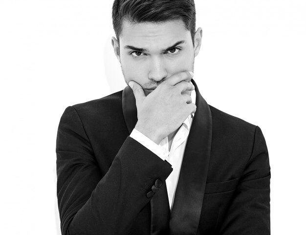 portrait of handsome fashion stylish businessman model dressed in elegant black classic suit. Touching his chin