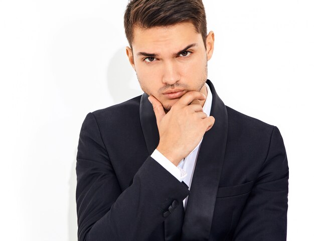 portrait of handsome fashion stylish businessman model dressed in elegant black classic suit. Touching his chin