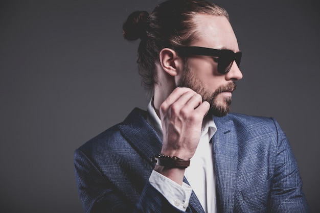portrait of handsome fashion stylish hipster businessman model dressed in elegant blue suit on gray