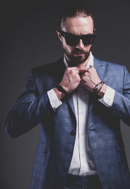 portrait of handsome fashion stylish hipster businessman model dressed in elegant blue suit posing on gray