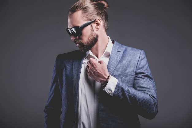 portrait of handsome fashion stylish hipster businessman model dressed in elegant blue suit posing on gray