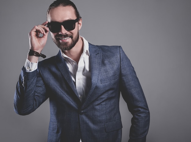 portrait of handsome fashion stylish hipster businessman model dressed in elegant blue suit posing on gray