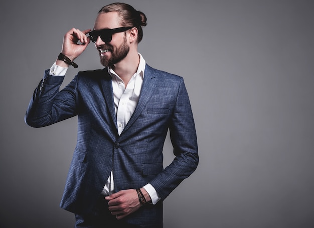 portrait of handsome fashion stylish hipster businessman model dressed in elegant blue suit posing on gray