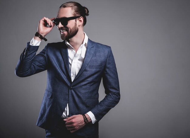 portrait of handsome fashion stylish hipster businessman model dressed in elegant blue suit posing on gray