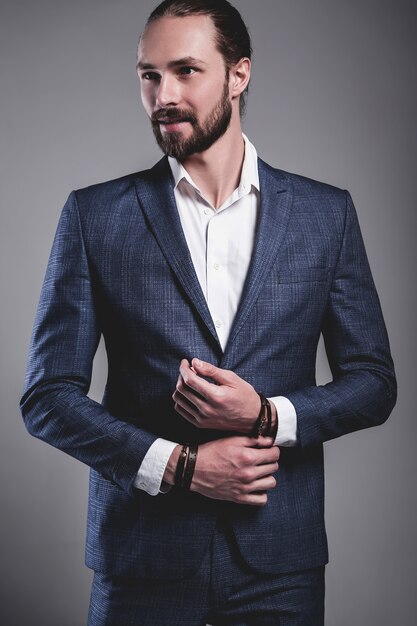 portrait of handsome fashion stylish hipster businessman model dressed in elegant blue suit posing on gray