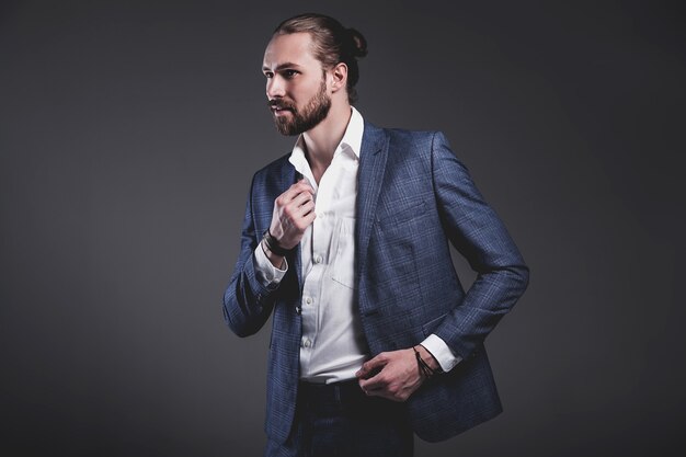 portrait of handsome fashion stylish hipster businessman model dressed in elegant blue suit posing on gray