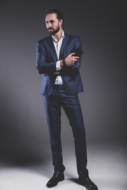 portrait of handsome fashion stylish hipster businessman model dressed in elegant blue suit  posing on gray