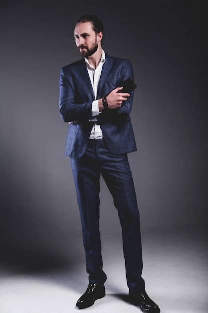 Портрет красивый модный стильный битник бизнесмен модель, одетый в элегантный синий костюм позирует на сером