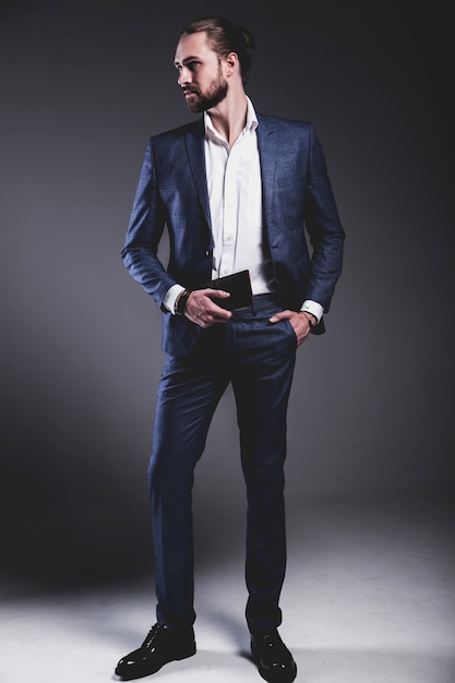 Foto gratuita il ritratto del modello dell'uomo d'affari alla moda dei pantaloni a vita bassa alla moda bello si è vestito in vestito blu elegante che posa sul gray