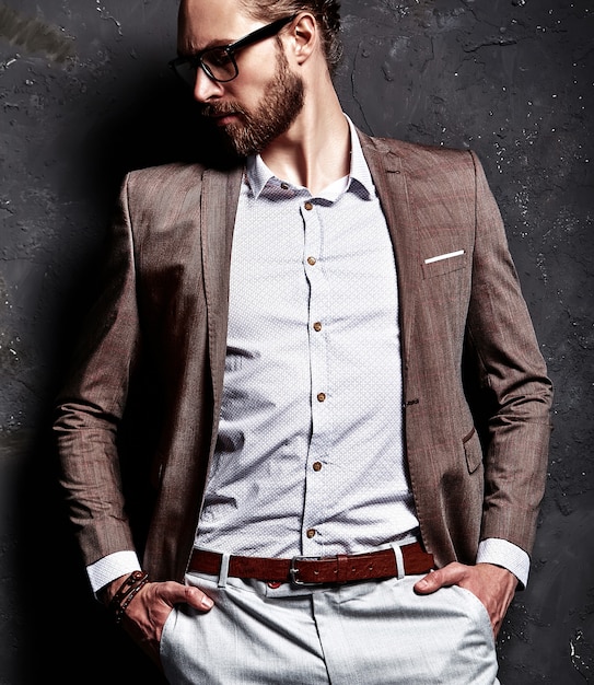 Портрет красивого модного стильного хипстерского бизнесмена, одетого в элегантный коричневый костюм в очках у темной стены