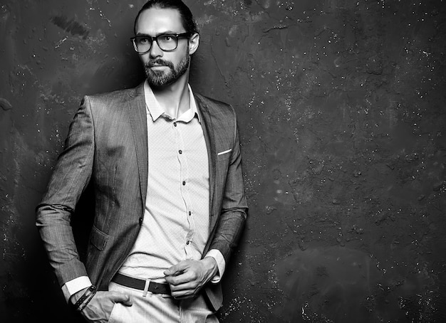 portrait of handsome fashion stylish hipster businessman model dressed in elegant brown suit in glasses  near dark wall